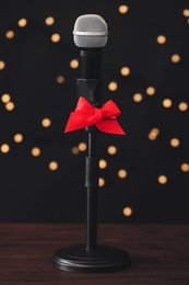 Photo of Microphone with red bow on wooden table against blurred lights. Christmas music