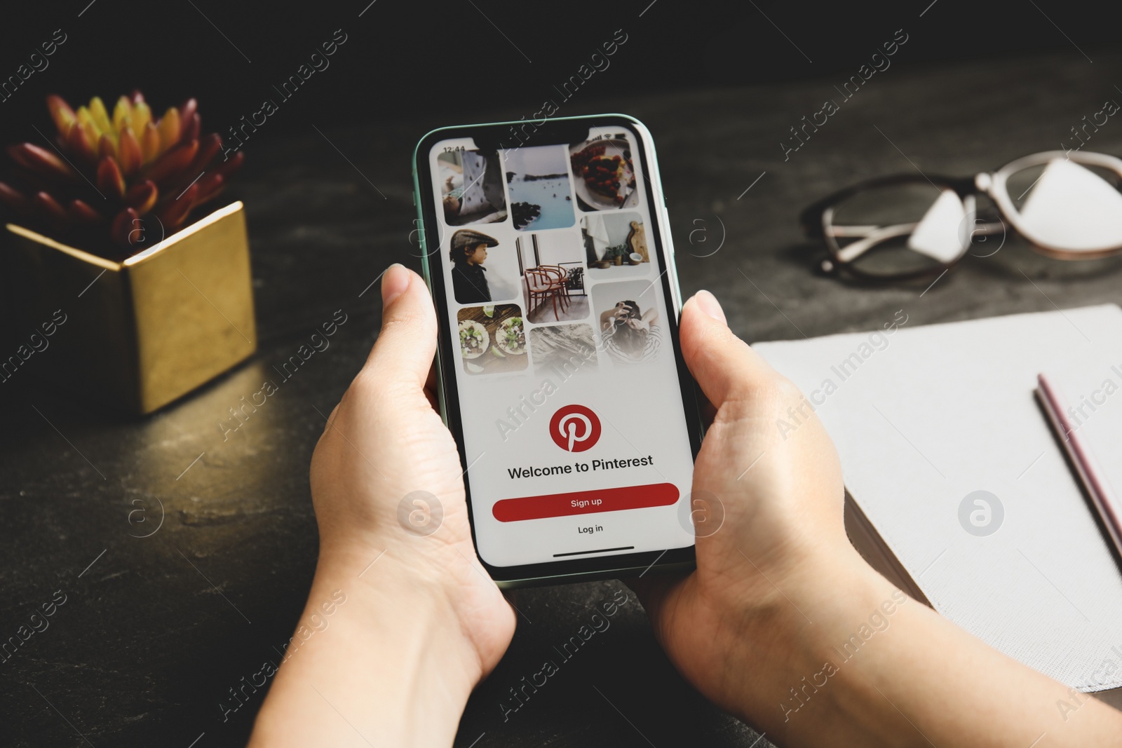 Photo of MYKOLAIV, UKRAINE - JULY 9, 2020: Woman holding Iphone 11 with Pinterest app on screen at table, closeup