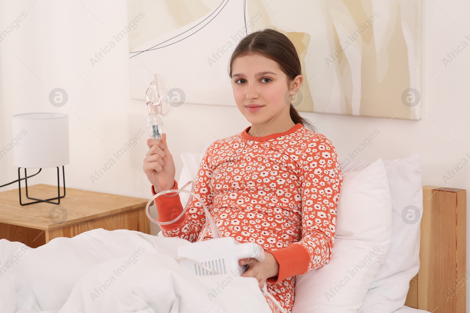 Photo of Cute girl holding nebulizer for inhalation on bed at home