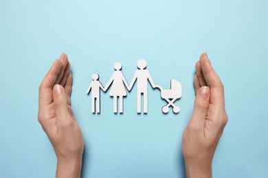 Photo of Woman protecting figures of family and heart on light blue background, top view. Insurance concept