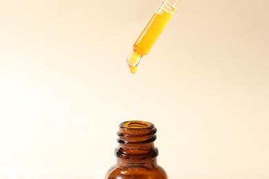 Dripping cosmetic serum from pipette into bottle on beige background, closeup