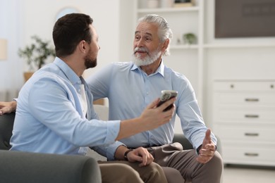 Happy son with smartphone and his dad on sofa at home