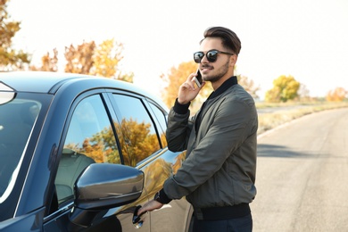 Young man talking on phone while opening car door, outdoors