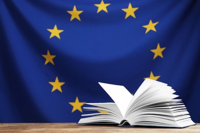 Photo of Open book on wooden table against flag of European Union. Space for text