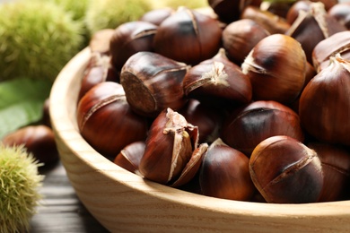 Photo of Delicious roasted edible chestnuts in wooden bowl on table, closeup
