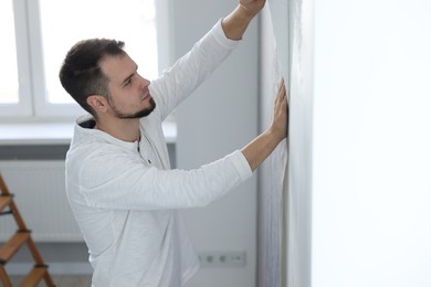 Photo of Man hanging stylish gray wallpaper in room