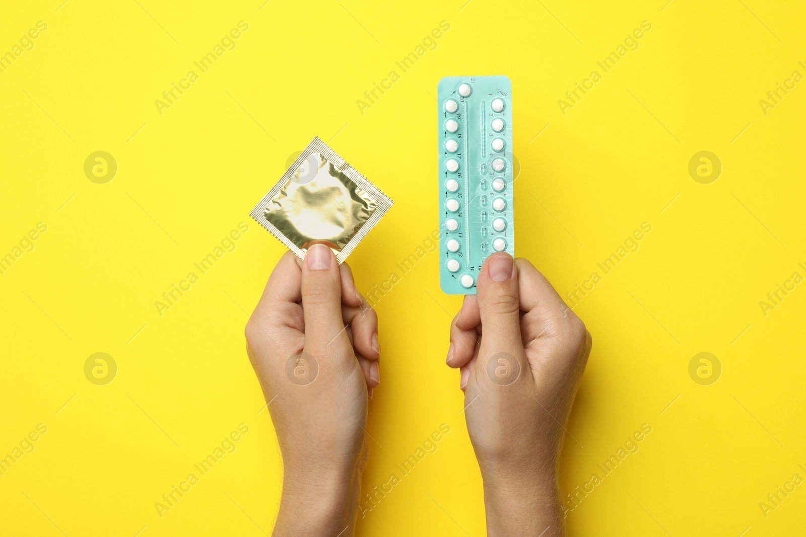 Photo of Woman holding condom and birth control pills on yellow background, top view. Safe sex