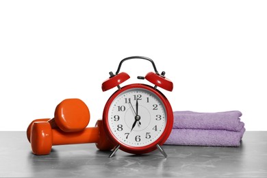 Photo of Alarm clock, towels and dumbbells on marble table against grey background. Morning exercise