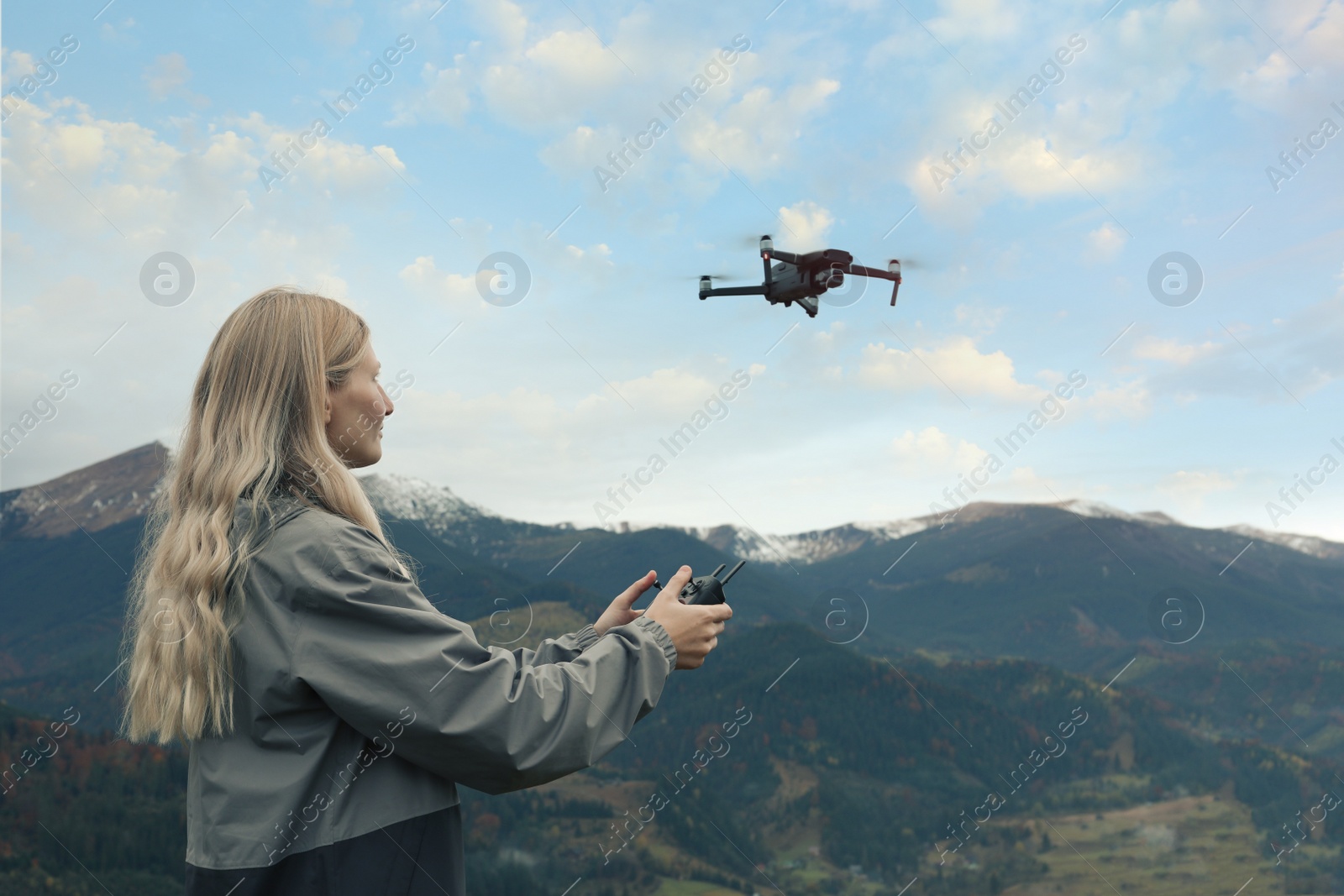 Photo of Young woman operating modern drone with remote control in mountains