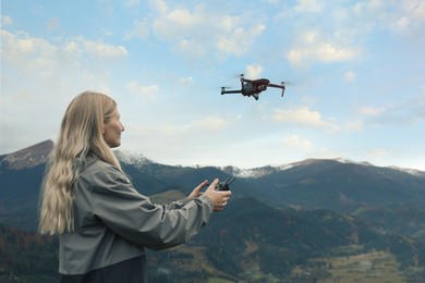 Young woman operating modern drone with remote control in mountains