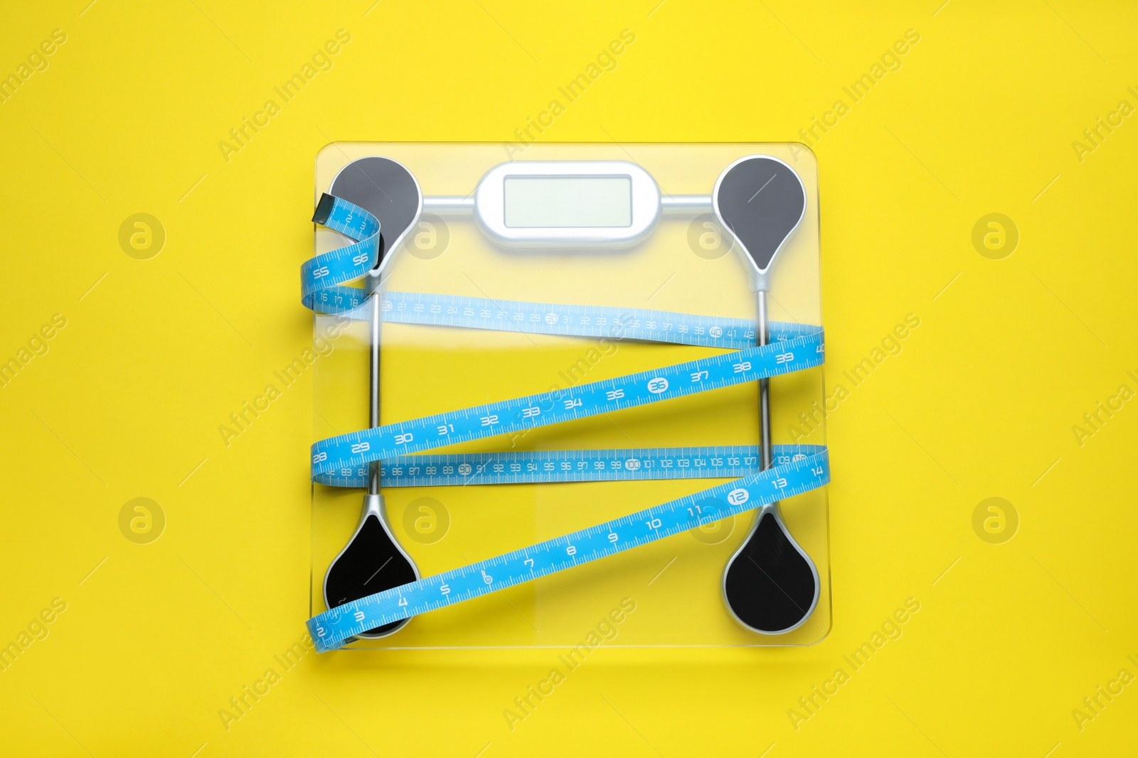 Photo of Electronic scales and measuring tape on yellow background, top view