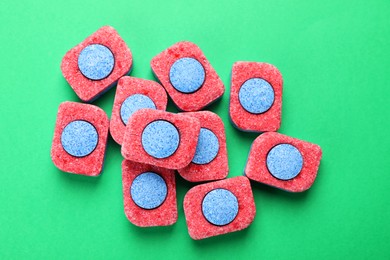 Photo of Many dishwasher detergent tablets on green background, flat lay