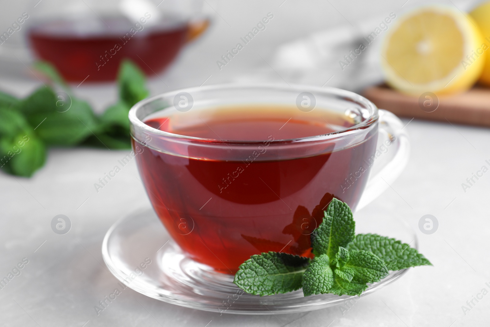 Photo of Cup of hot aromatic tea with mint on light grey marble table, closeup