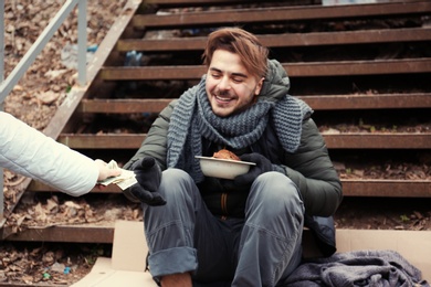 Poor young man begging for money on stairs outdoors, closeup