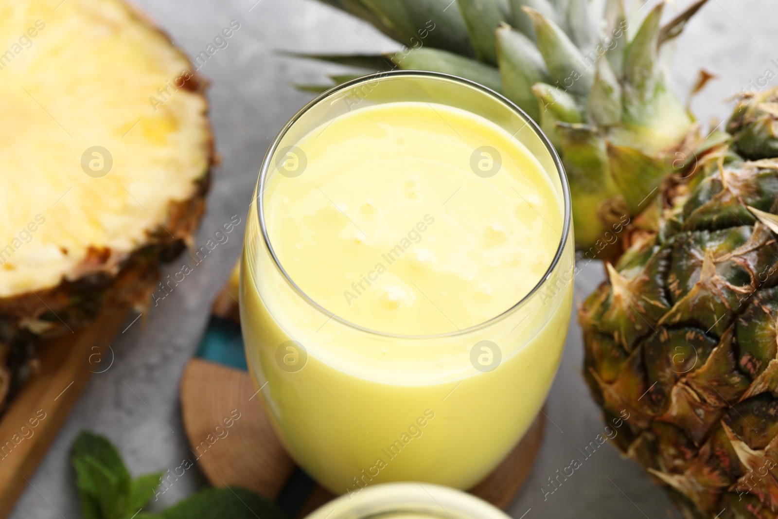 Photo of Tasty pineapple smoothie, mint and fruit on grey textured table, closeup