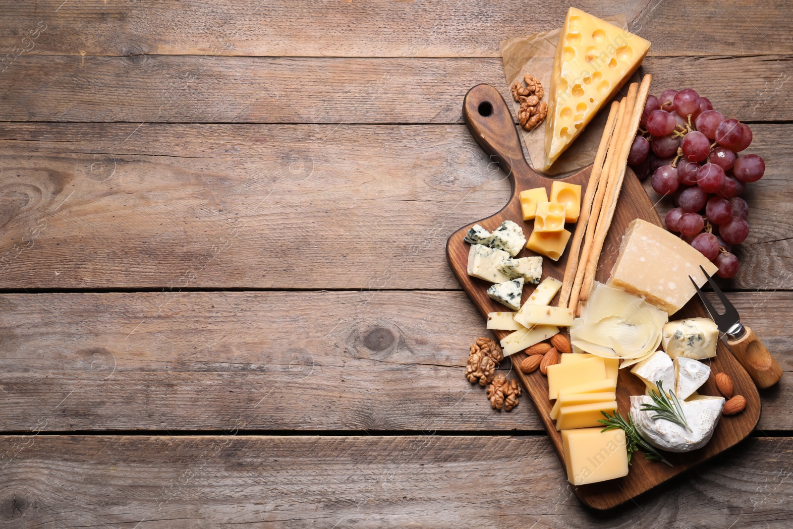 Photo of Cheese plate with grapes and nuts on wooden table, top view. Space for text