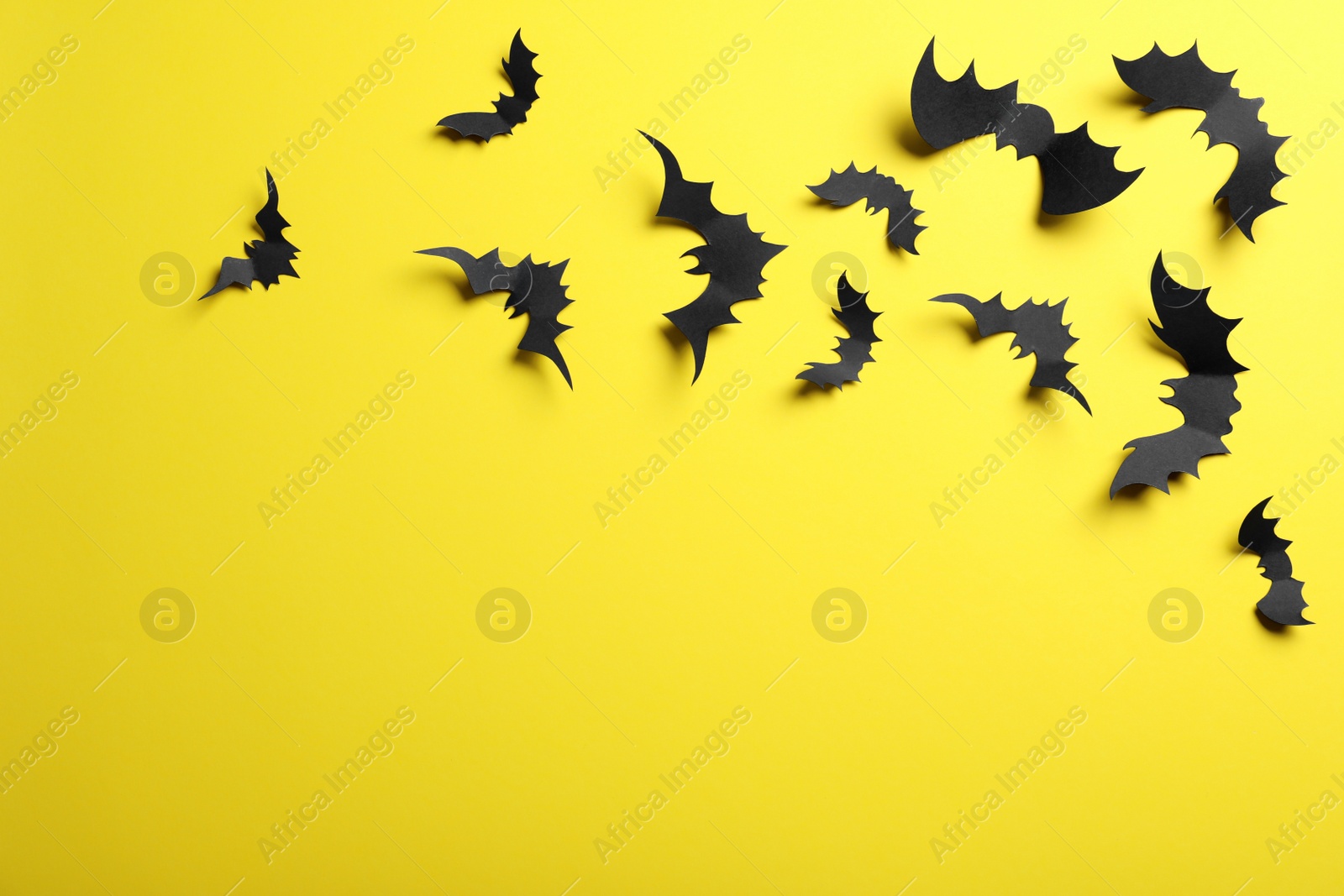 Photo of Paper bats on yellow background, flat lay with space for text. Halloween decor