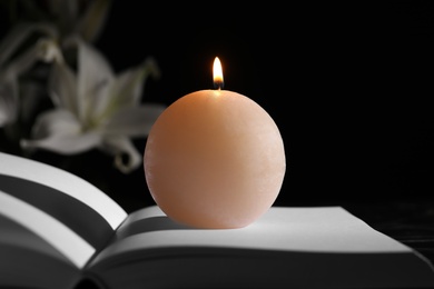 Burning candle on book in darkness. Funeral symbol