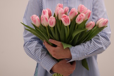 Woman with bouquet of beautiful fresh tulips on light grey background, closeup