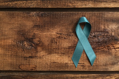 Photo of Teal awareness ribbon on wooden background, top view with space for text. Symbol of social and medical issues
