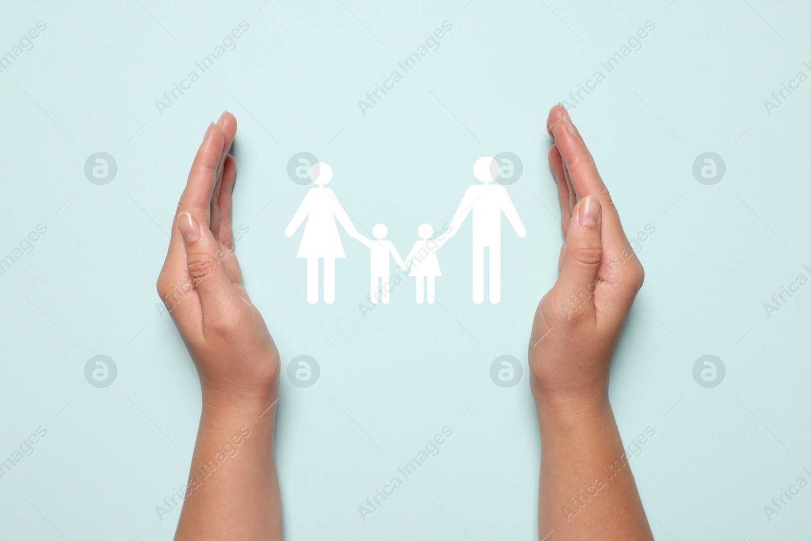 Image of Woman holding hands around paper silhouette of family on light blue background, top view. Insurance concept