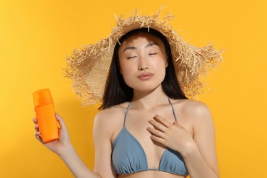 Photo of Beautiful young woman in straw hat holding sun protection cream on orange background