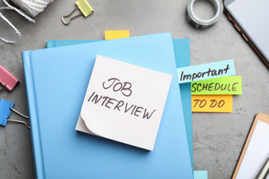 Photo of Reminder note about job interview and stationery on table, flat lay