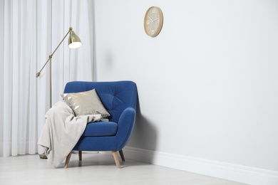 Photo of Stylish armchair with pillow and plaid near white wall, space for text. Interior design
