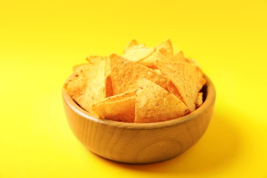 Photo of Tasty mexican nachos chips in wooden bowl on yellow background