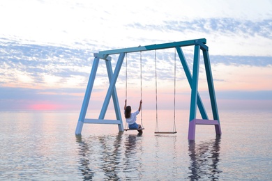 Photo of Young woman enjoying sunrise on swing over water