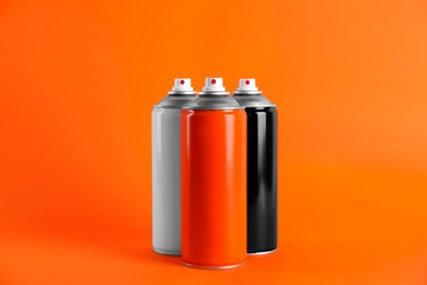 Photo of Colorful cans of spray paints on orange background