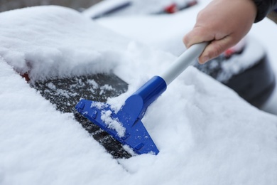 Photo of Man cleaning snow from car outdoors on winter day, closeup. Frosty weather