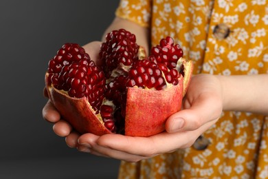 Photo of Woman holding fresh pomegranate on dark background, closeup