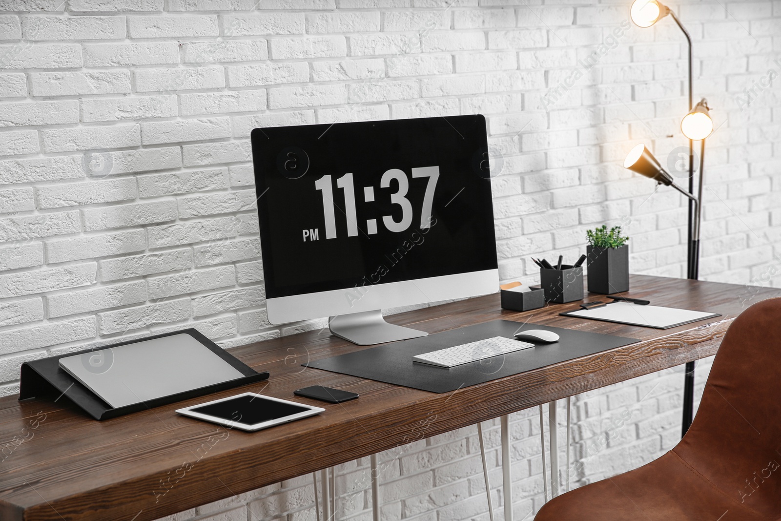 Photo of Modern workplace interior with computer and devices on table near brick wall