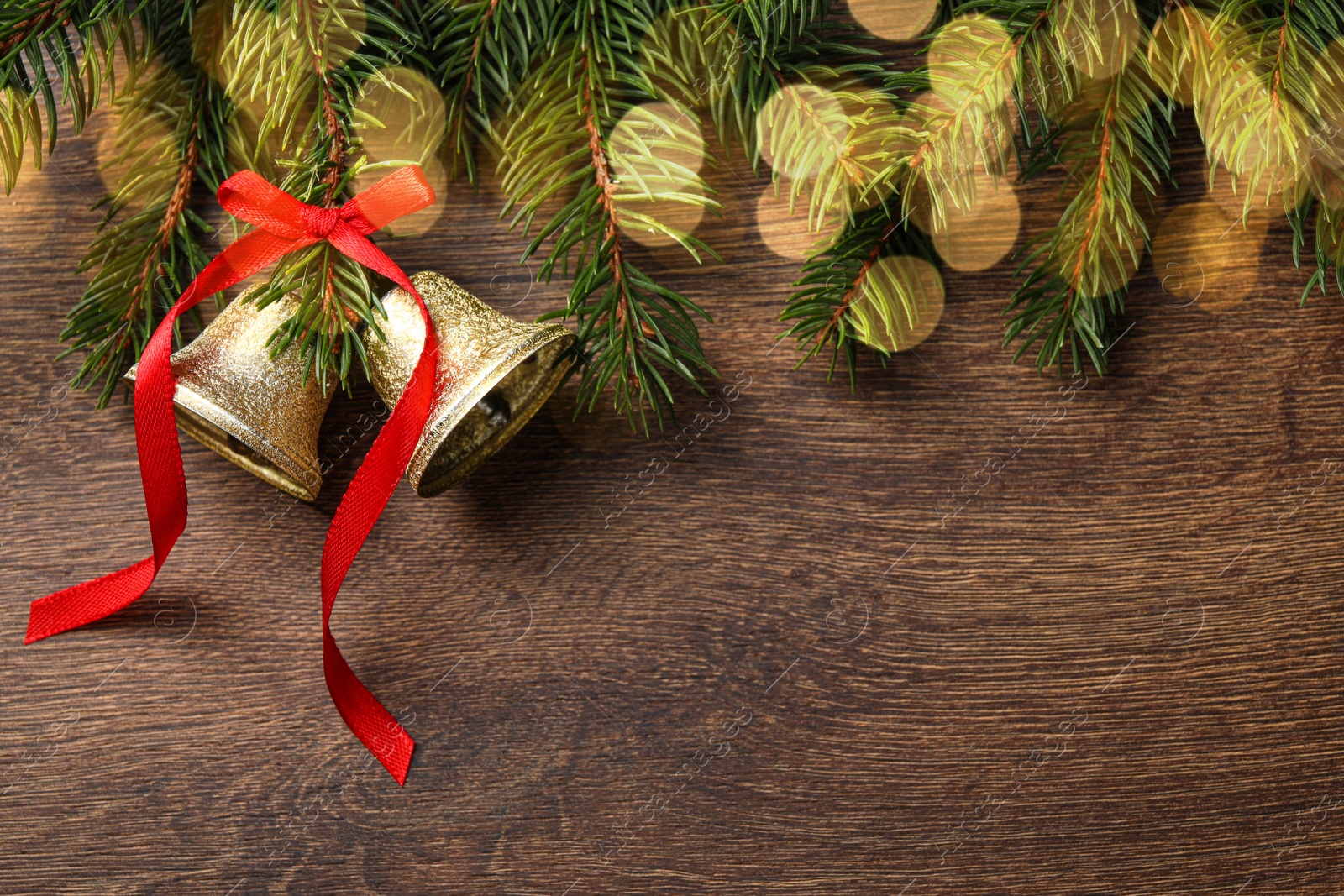 Photo of Christmas bells and fir tree branches on wooden table, flat lay. Space for text