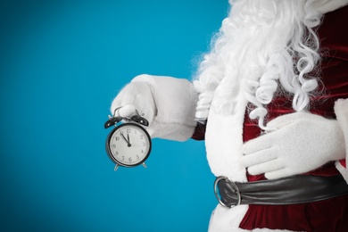 Photo of Santa Claus holding alarm clock on blue background, closeup. Christmas countdown