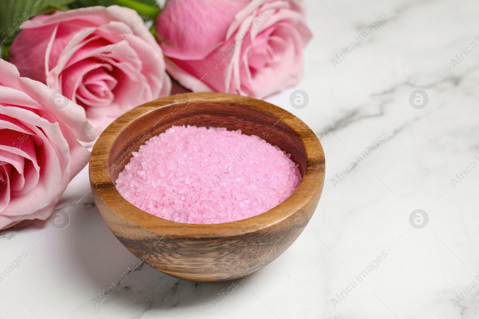 Photo of Wooden bowl with pink sea salt and beautiful roses on white marble table