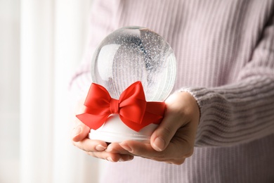 Photo of Woman holding empty snow globe with red bow indoors, closeup. Space for text