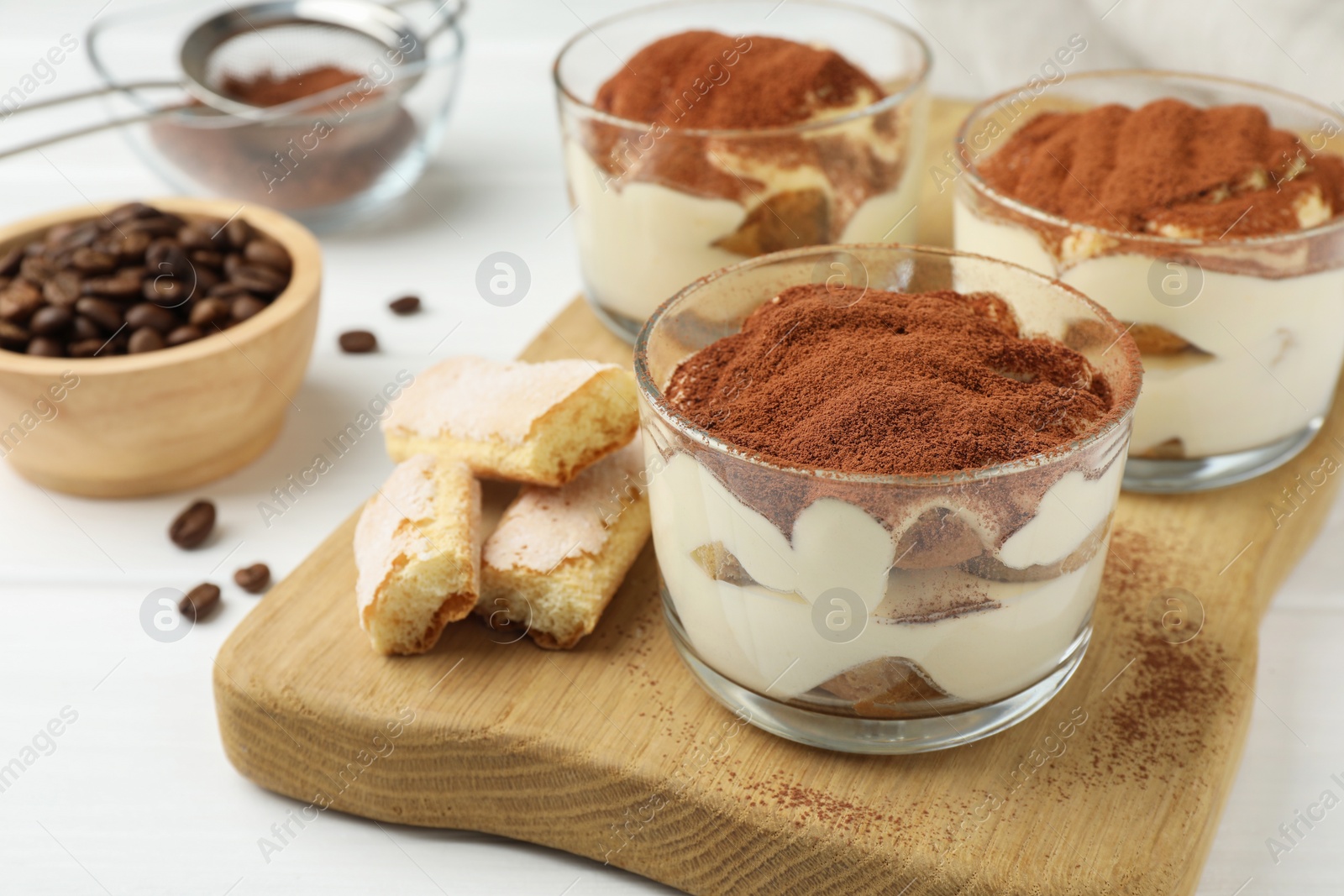 Photo of Delicious tiramisu in glasses, cookies and coffee beans on white table, closeup