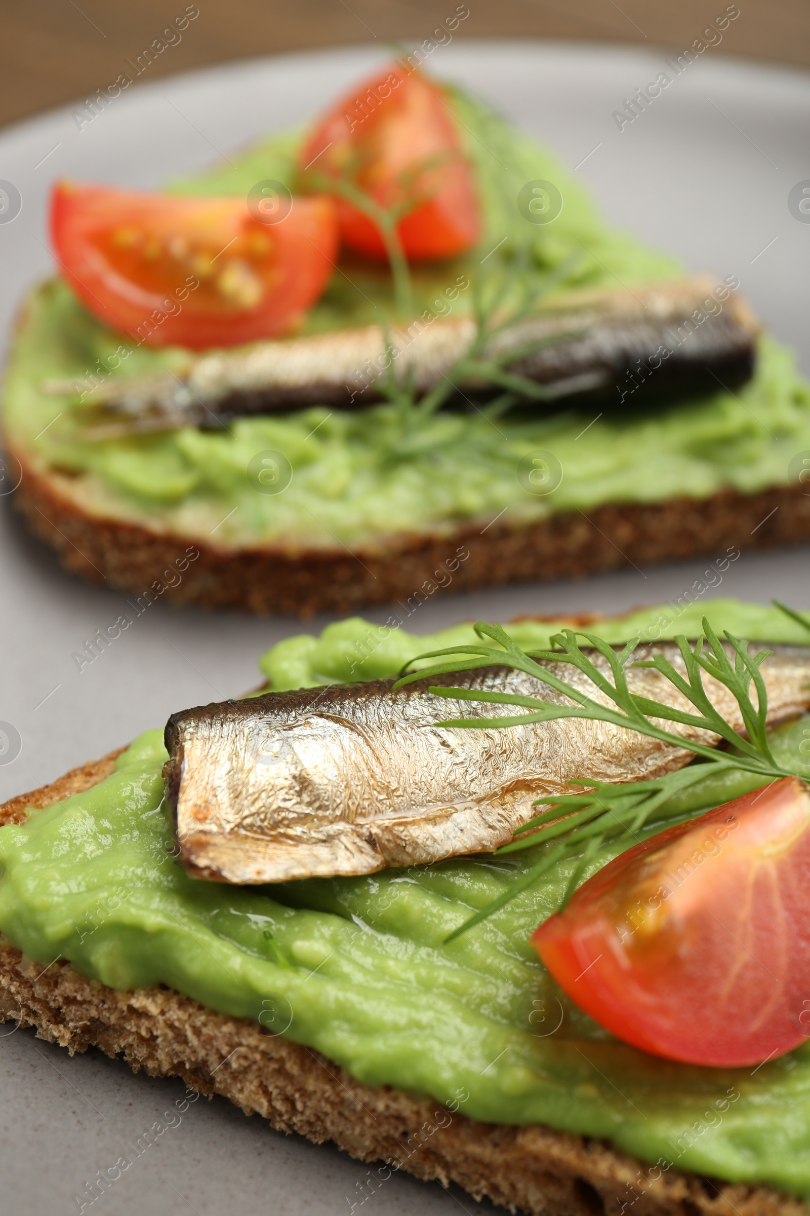 Delicious sandwiches with sprats, tomatoes, avocado puree and dill on plate, closeup Photo of Delicious sandwiches with sprats, tomatoes, avocado puree and dill on plate, closeup
