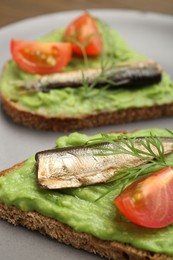 Photo of Delicious sandwiches with sprats, tomatoes, avocado puree and dill on plate, closeup