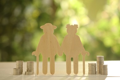 Photo of Pension savings. Figure of senior couple and stacked coins on white wooden table outdoors