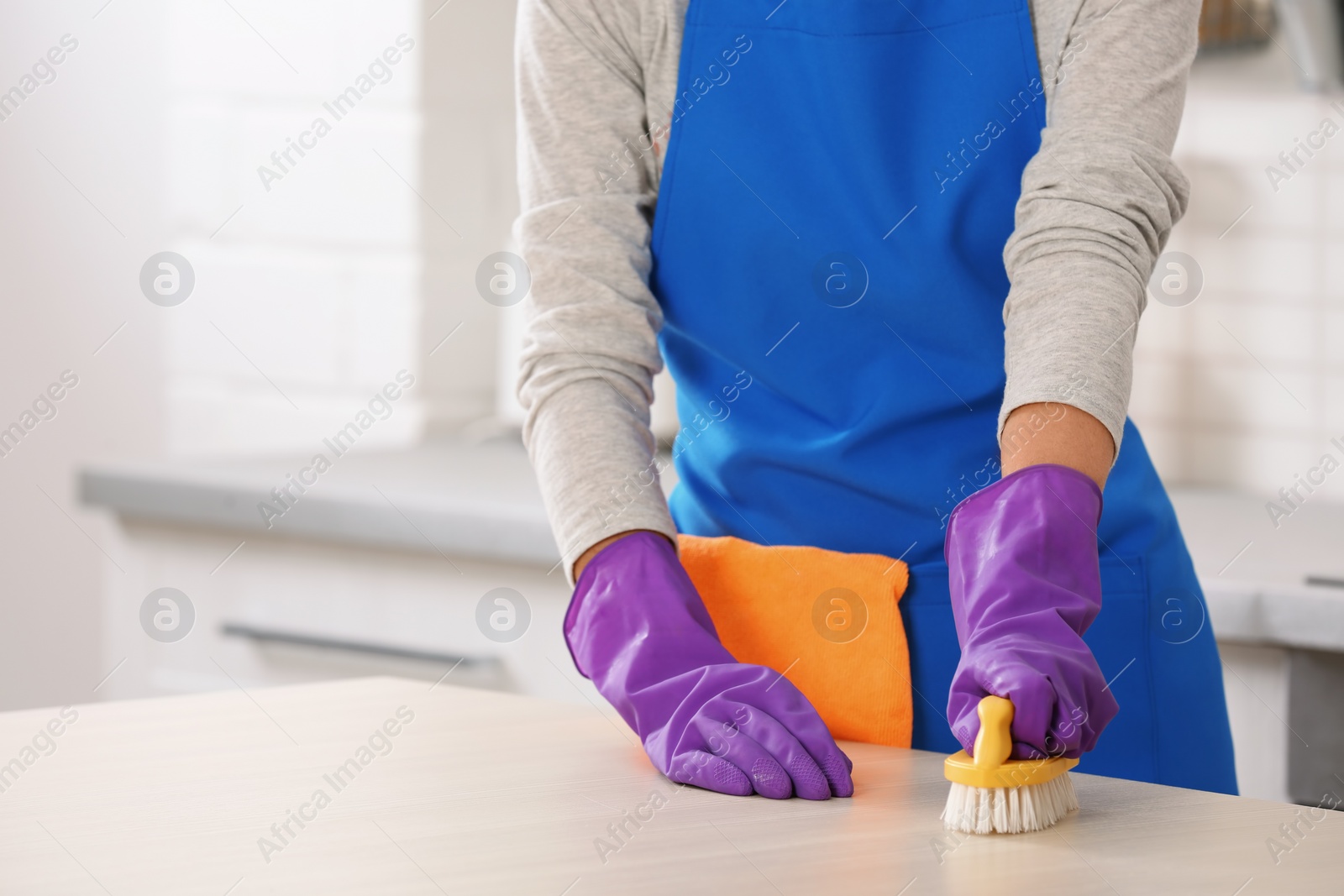 Photo of Woman cleaning table with brush in kitchen, closeup. Space for text