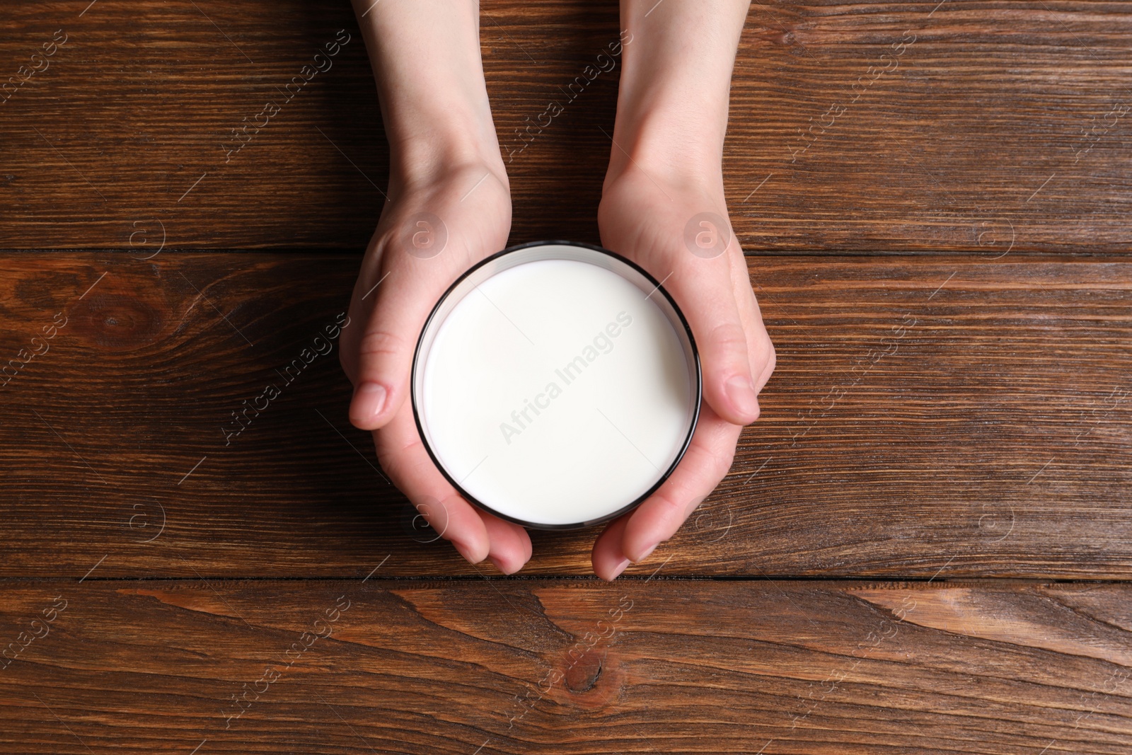 Photo of Woman holding glass of milk at wooden table, top view