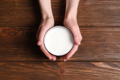 Photo of Woman holding glass of milk at wooden table, top view