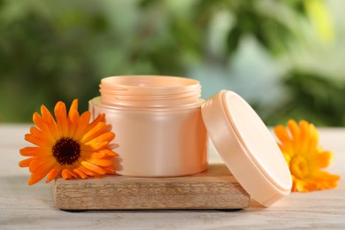 Jar of cream and beautiful calendula flowers on white wooden table outdoors, closeup