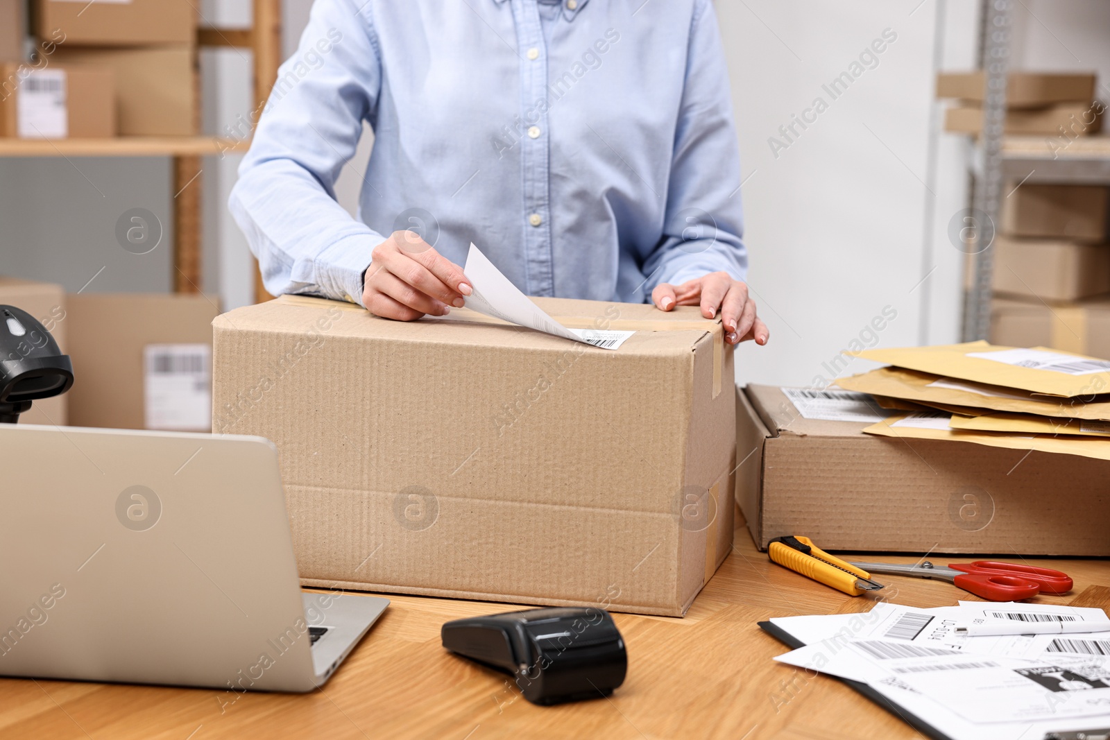 Photo of Parcel packing. Post office worker sticking barcode on box at wooden table indoors, closeup