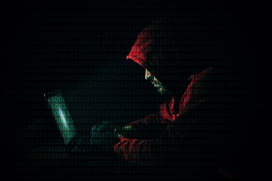 Image of Anonymous man with laptop and binary code in darkness