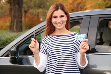 Happy woman holding driving license near car