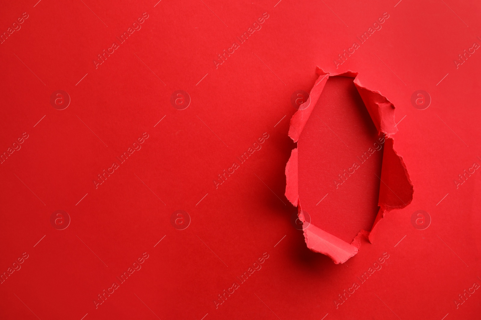 Photo of Hole in red paper on color background, space for text